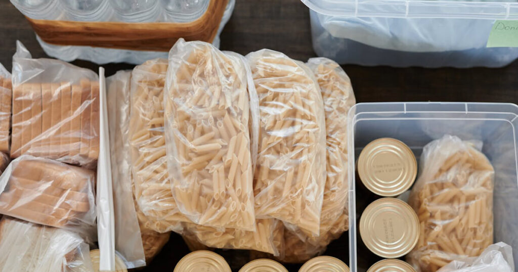 An organized assortment of pantry staples, including bags of dried pasta, canned goods, and neatly stacked crackers, all stored in clear plastic bags and containers. The arrangement conveys a sense of order and preparedness, highlighting a clean and well-maintained pantry space.