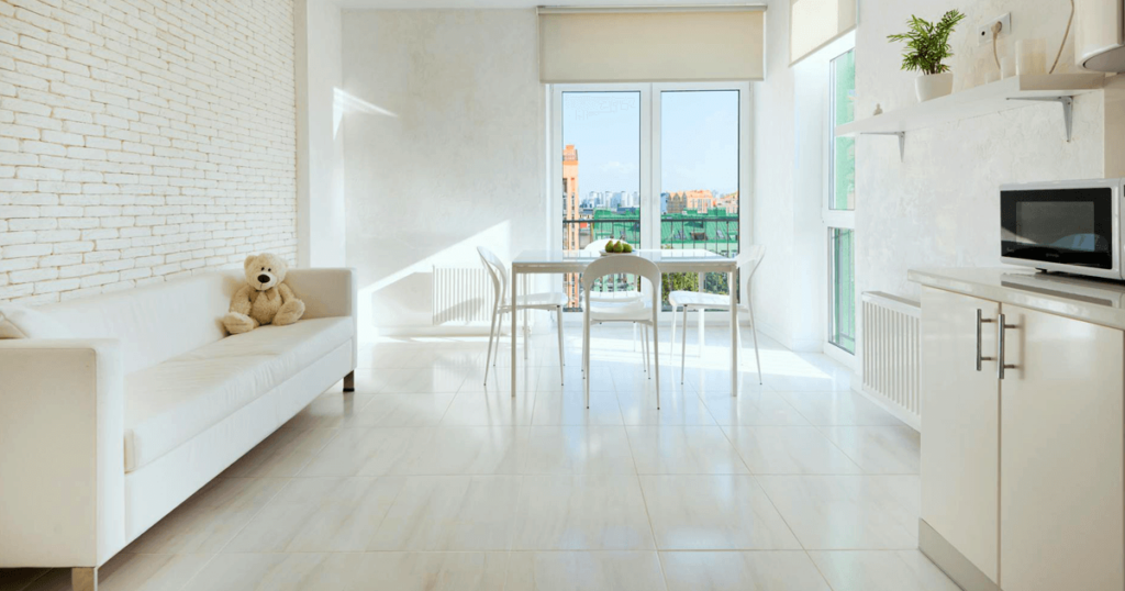 Bright and airy small living space with large windows letting in natural light, featuring a white sofa, a minimalist dining table with chairs, and light-colored flooring that enhances the sense of openness.