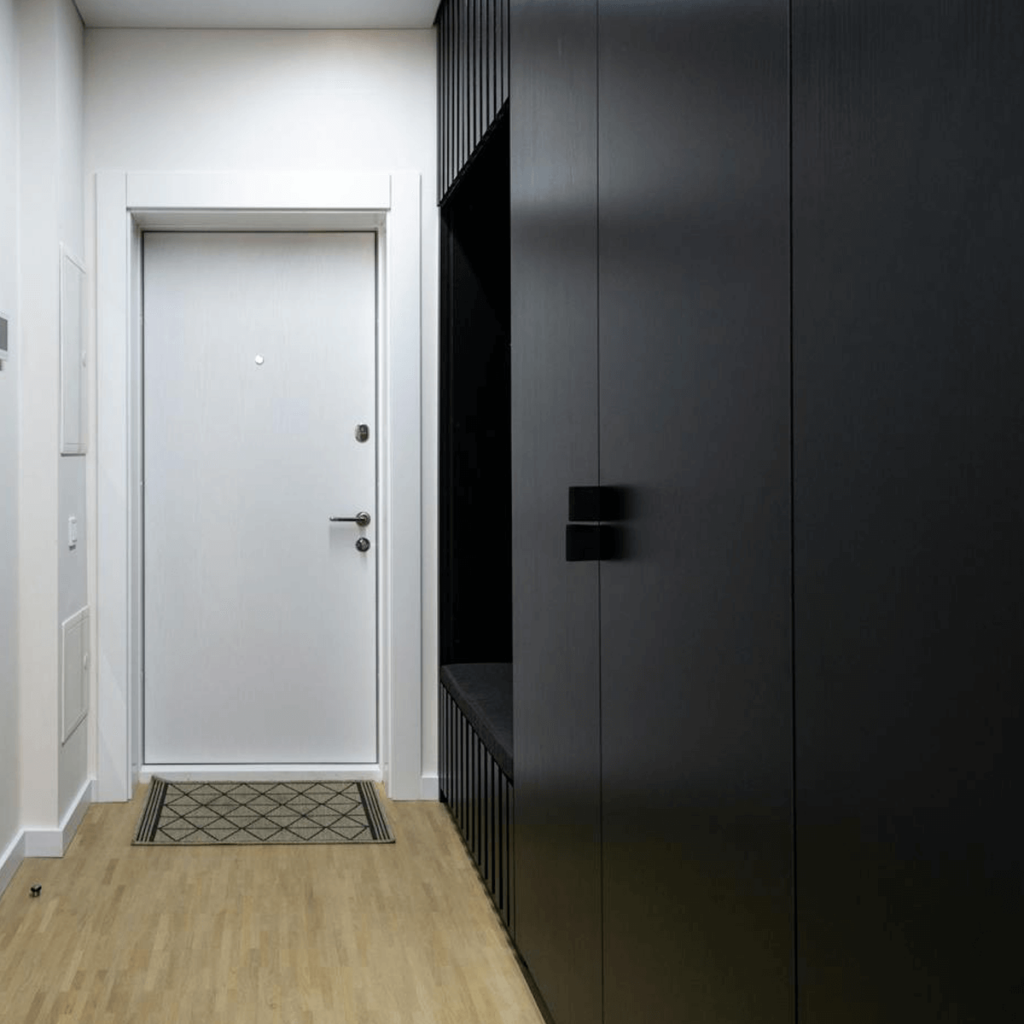Modern small entryway with a white door, light wood flooring, and sleek black built-in storage cabinets, showcasing practical space-saving solutions for compact hallways.