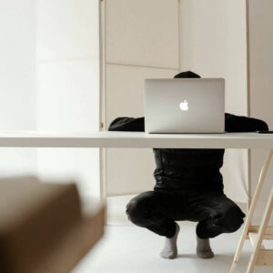 A minimalist workspace featuring a laptop on a clean white desk. The person seated behind the desk is partially hidden, emphasizing focus and simplicity. The neutral tones and uncluttered environment convey productivity and intentionality.