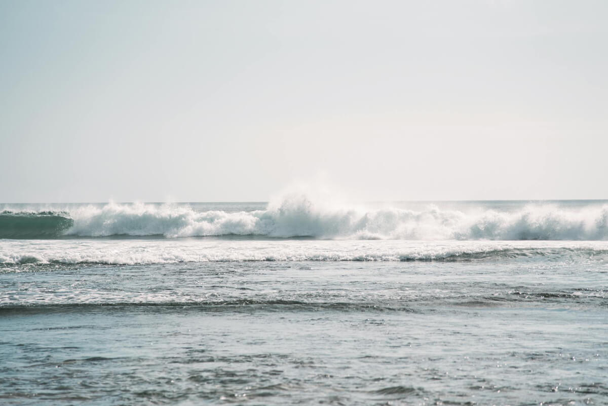 A serene ocean scene with gentle waves rolling steadily toward the shore under a soft, pale sky. The rhythmic movement of the water reflects the power of consistency and persistence, evoking a sense of calm and determination. With time and consistency, achieving your goals is possible.