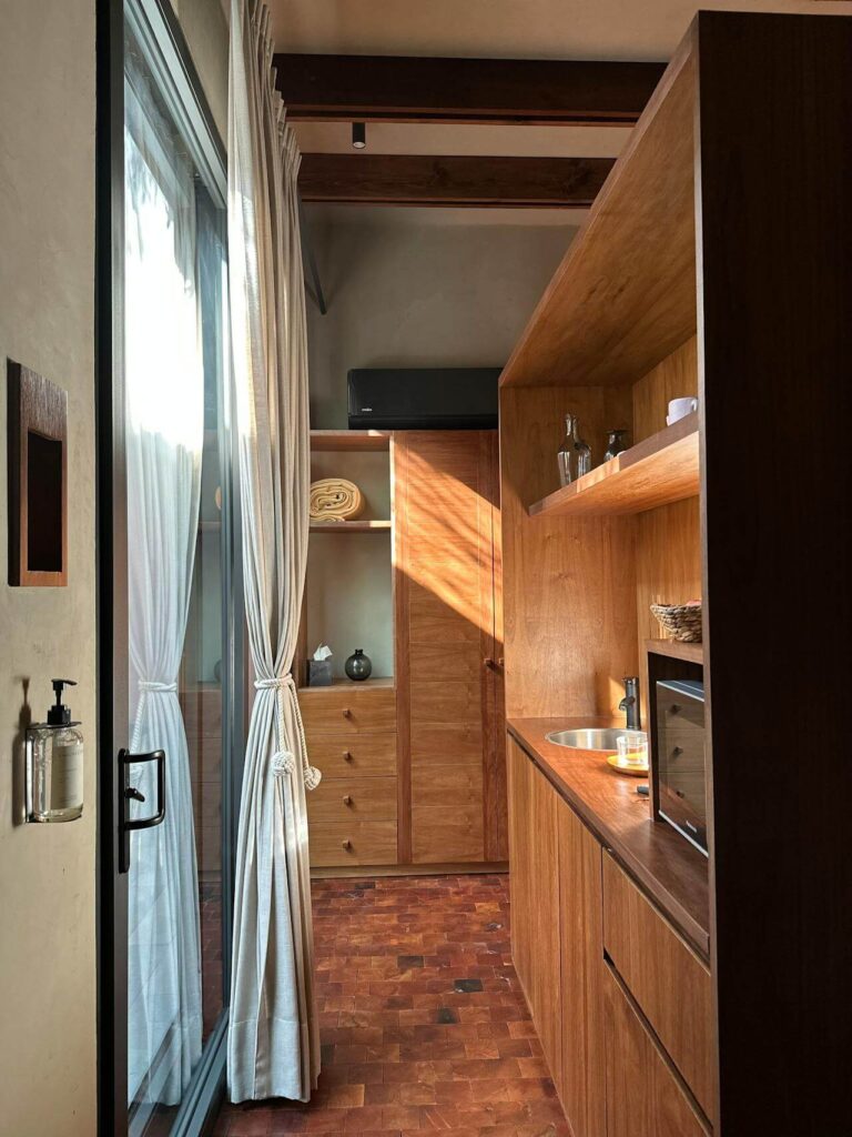 Cozy small kitchen with warm wood cabinetry, a compact sink, built-in microwave, and open shelving, all illuminated by natural light from a large sliding glass door. Inspiring layout for tiny kitchens with limited space.