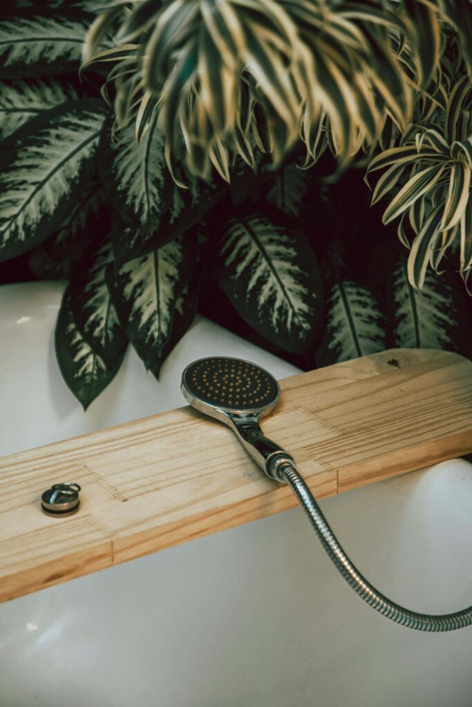 Handheld showerhead resting on a wooden bath tray surrounded by lush green houseplants, evoking a peaceful, minimalist atmosphere that reflects slow living and the calming simplicity of a thoughtfully designed home.