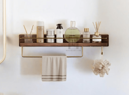 Wall-mounted wooden bathroom shelf with gold accents, holding various toiletries, a towel, and a bath sponge, demonstrating organized storage solutions for maximizing space in a small bathroom.