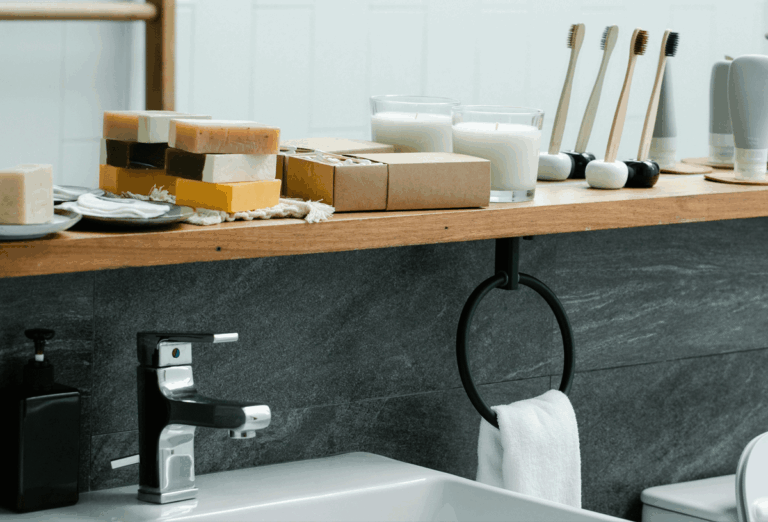 Bathroom storage ideas for small spaces shown on the photo. A well-organized bathroom countertop displaying neatly stacked handmade soaps, candles, boxed items, and bamboo toothbrushes with holders, showcasing smart and stylish storage ideas for small bathroom spaces.