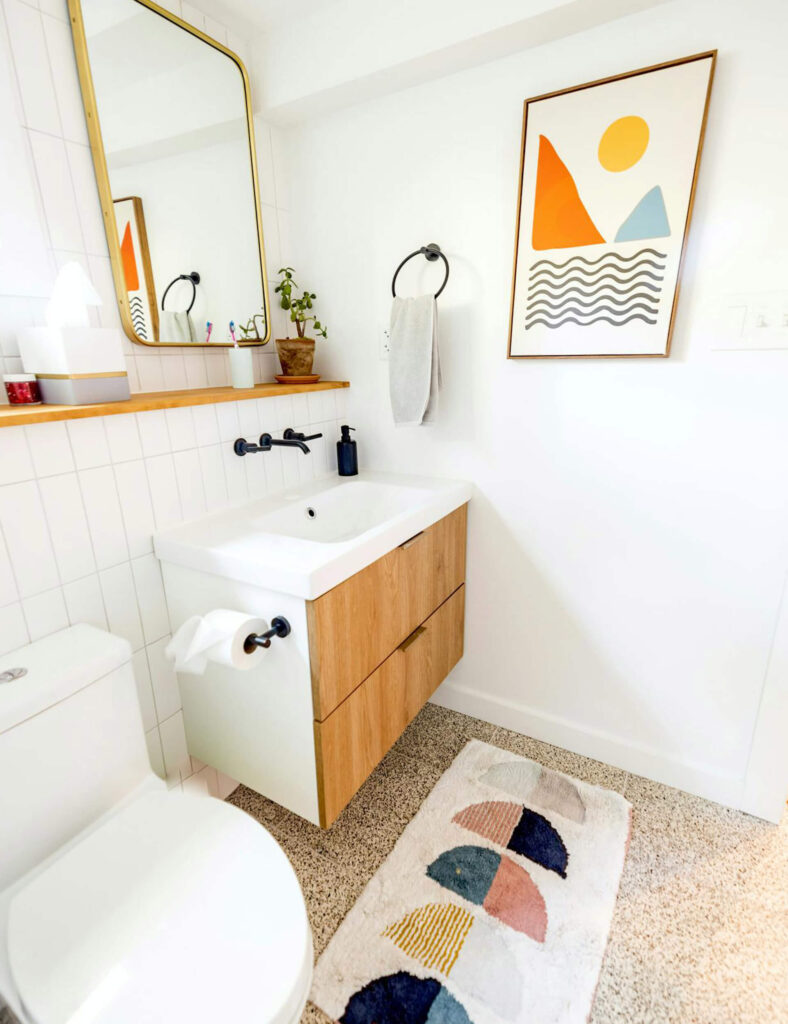 Bright, modern bathroom with a compact vanity, open shelf, and decorative art, featuring smart use of wall and floor space.
