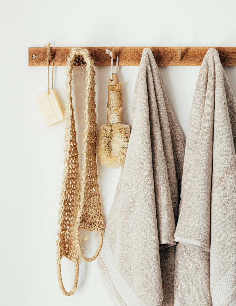 Wooden wall hooks neatly holding bath towels, a brush, a soap bar, and a woven bath mitt, demonstrating efficient small bathroom storage.