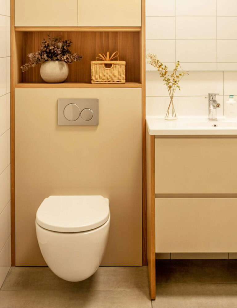 Bathroom with a wall-mounted toilet set beneath a wooden shelf displaying a vase and a small wicker basket.