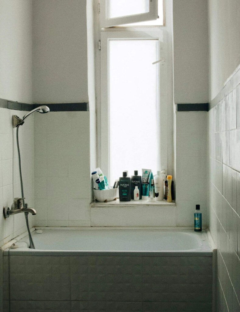Bathroom with a bathtub and shower, displaying various toiletries and bottles neatly arranged on the window ledge above the tub.
