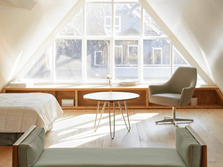 Minimalist small attic bedroom with slanted ceiling, featuring sleek furniture, a cozy reading chair, and soft natural light for a tranquil retreat. Small attic bedroom ideas are visible, like the built-in storages, airy bedroom layout.