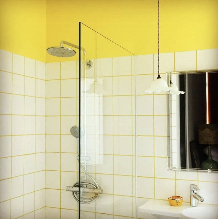 Contemporary bathroom shower with white subway tiles and pale yellow grout, accented by a yellow painted wall, chrome rainfall showerhead, glass divider, and a pendant light over the sink.