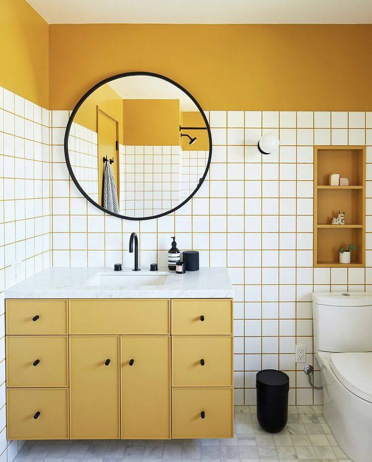 Chic bathroom with white subway wall tiles and mustard yellow grout, paired with a circular mirror, black fixtures, and matching yellow vanity cabinetry.