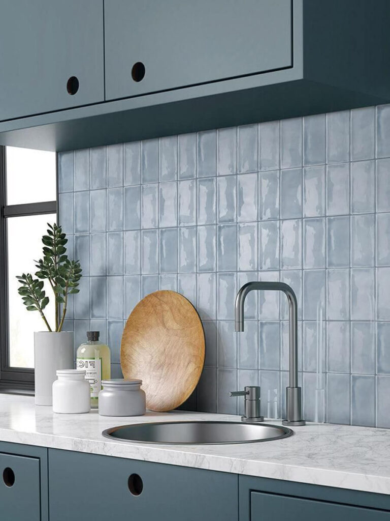 Matte blue tiles arranged in a vertical grid for a kitchen backsplash, paired with blue cabinetry, marble countertop, and metallic fixtures for a cool, cohesive look.