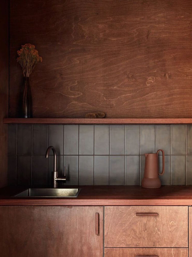 Tall matte grey tiles set in a vertical grid for a kitchen backsplash, surrounded by wood cabinetry and metal fixtures for a sleek, muted effect.