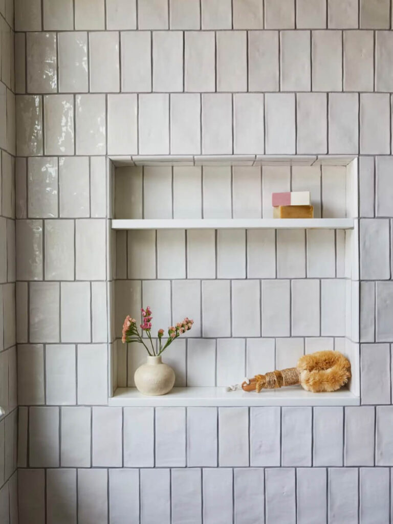 Vertical running bond white tile wall with matte finish, grey grout lines, and recessed shelving, styled with simple accessories for a serene washroom look.
