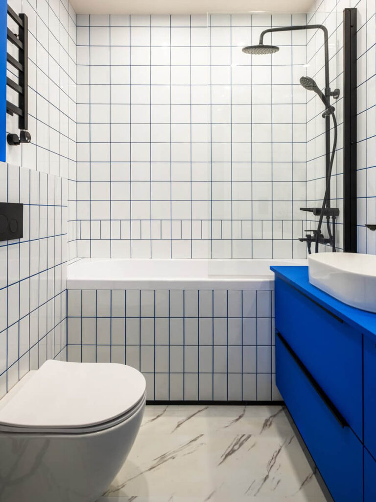 Bright bathroom featuring white subway tiles with blue grout in mixed horizontal and vertical patterns, bold blue vanity, and matte black fixtures.