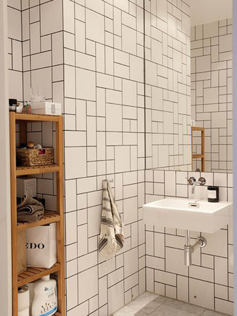 Minimalist bathroom with white mixed subway tiles, black grout, marble floor, glass shower enclosure, and modern fixtures for a geometric statement.