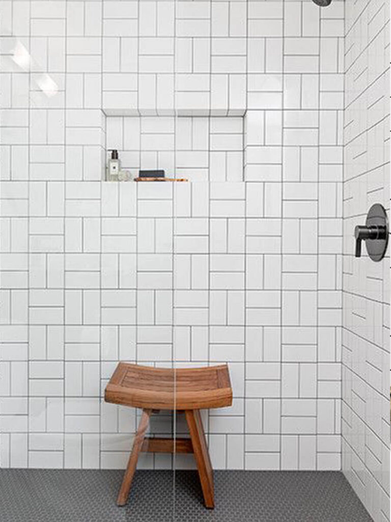 Bathroom wall with glossy white tiles laid in a basket weave pattern, accented by an inset niche with small hexagonal tiles and matte black fixtures for a crisp look.