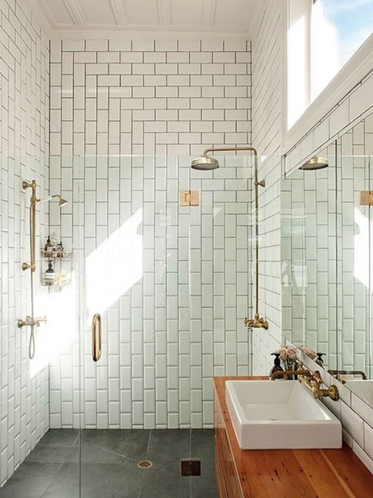 Modern bathroom featuring a walk-in shower with glossy subway tiles stacked in a vertical herringbone design, black tile floor, glass walls, wood vanity, and a large window for maximum light.