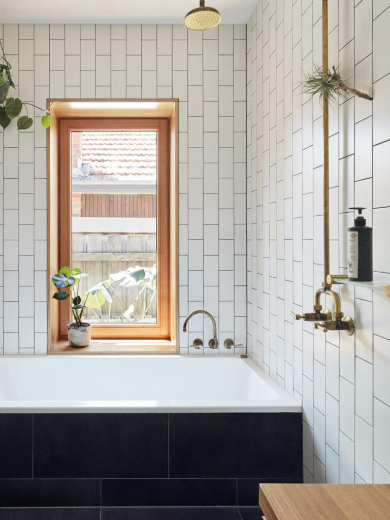 Bathroom with matte white subway tiles arranged in a simple vertical running bond pattern, paired with floating wood vanity, white sink, black fixtures, and subtle modern accents.
