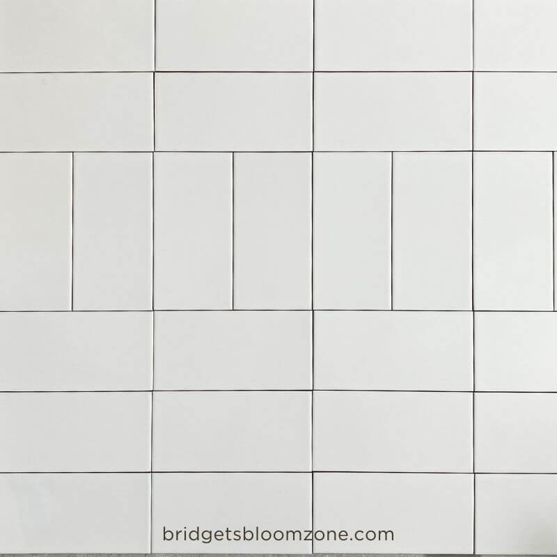 White rectangular subway tiles laid out on the floor in different patterns to test layout ideas for a small white bathroom.