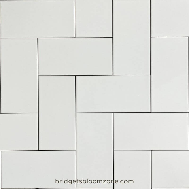 White rectangular subway tiles laid out on the floor in different patterns to test layout ideas for a small white bathroom.