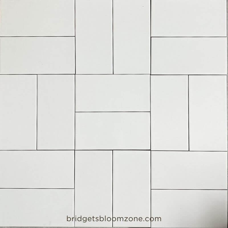 White rectangular subway tiles laid out on the floor in different patterns to test layout ideas for a small white bathroom.