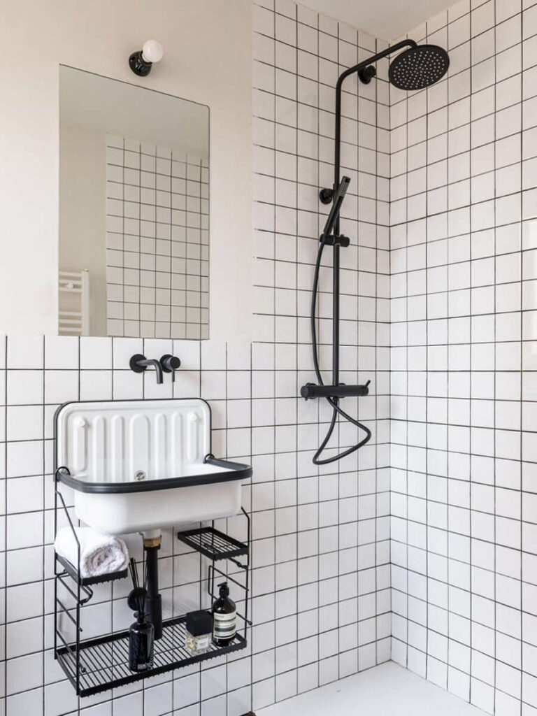 Minimalist bathroom shower with black hardware, white square tiles and black grout, a utility-style sink with black frame, and a large mirror.