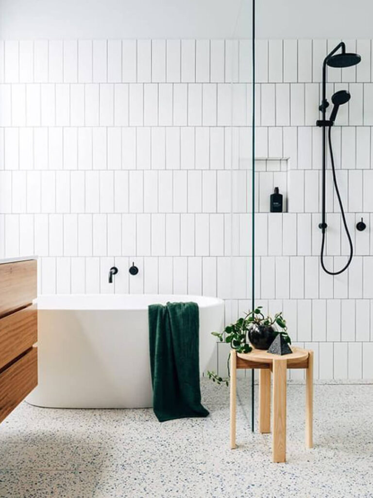 Contemporary bathroom featuring horizontal white tiles with gray grout, matte black fixtures, floating wood cabinetry, and terrazzo floor.