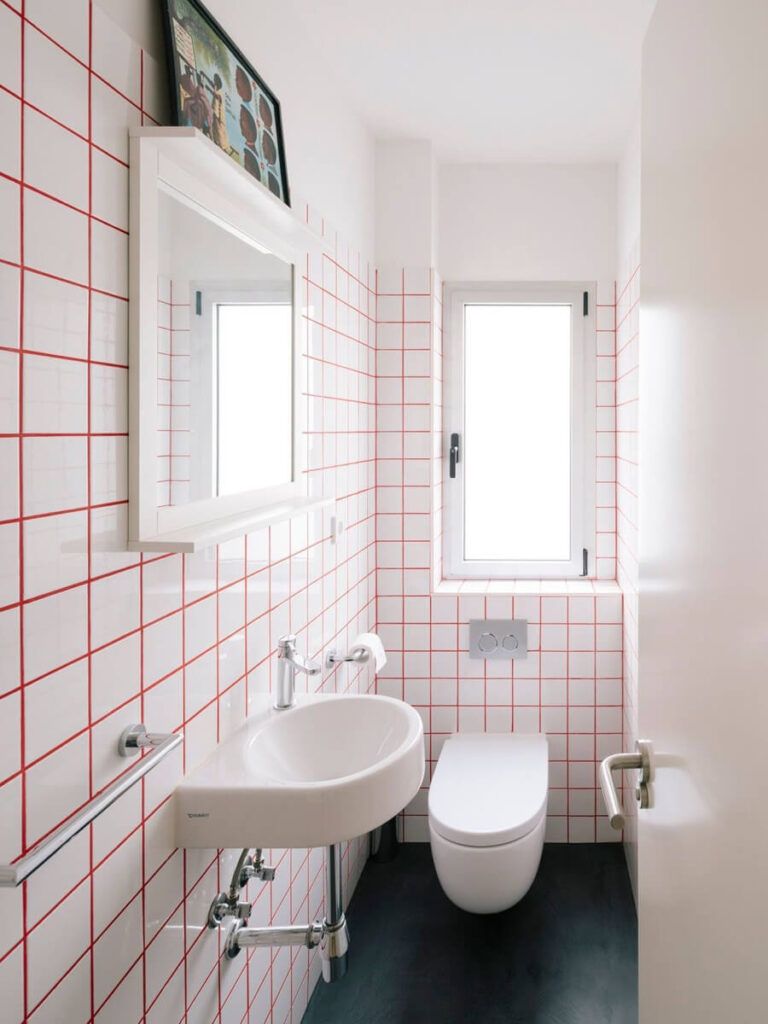 All-white bathroom with bold red grout on every wall, floating fixtures, and black flooring for a vivid, streamlined look.