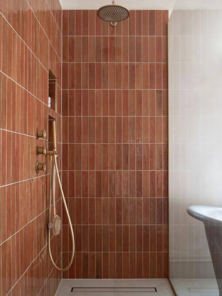 Shower with vertical terracotta tiles and brass fixtures, showcasing warm small bathroom color ideas and inviting earth-toned Bathroom Color Schemes.