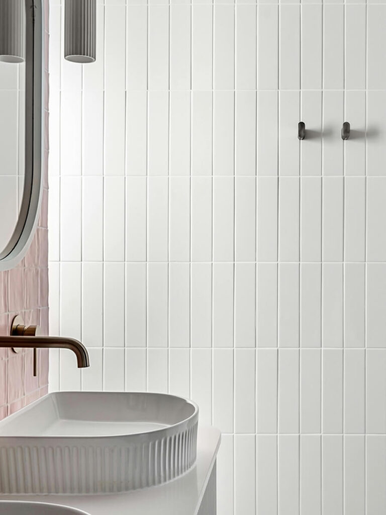 Minimal bathroom wall with vertical matte white tiles and subtle white grout, rounded fixtures, and soft contemporary styling.