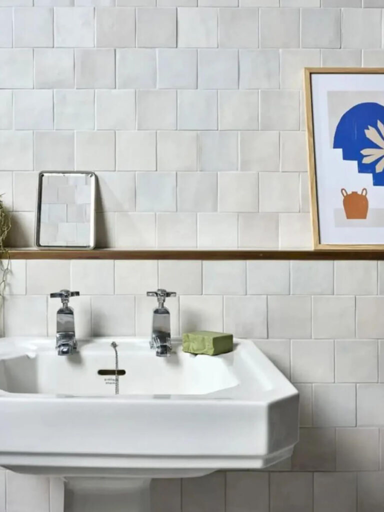 Retro bathroom sink area with hand-cut matte white tiles, white grout, minimal accessories, and contemporary artwork above the backsplash.