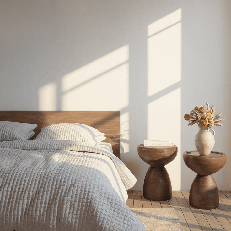 Modern bedroom with sculptural wooden bedside tables featuring curved hourglass shapes, holding decorative items and dried flowers in soft natural light.