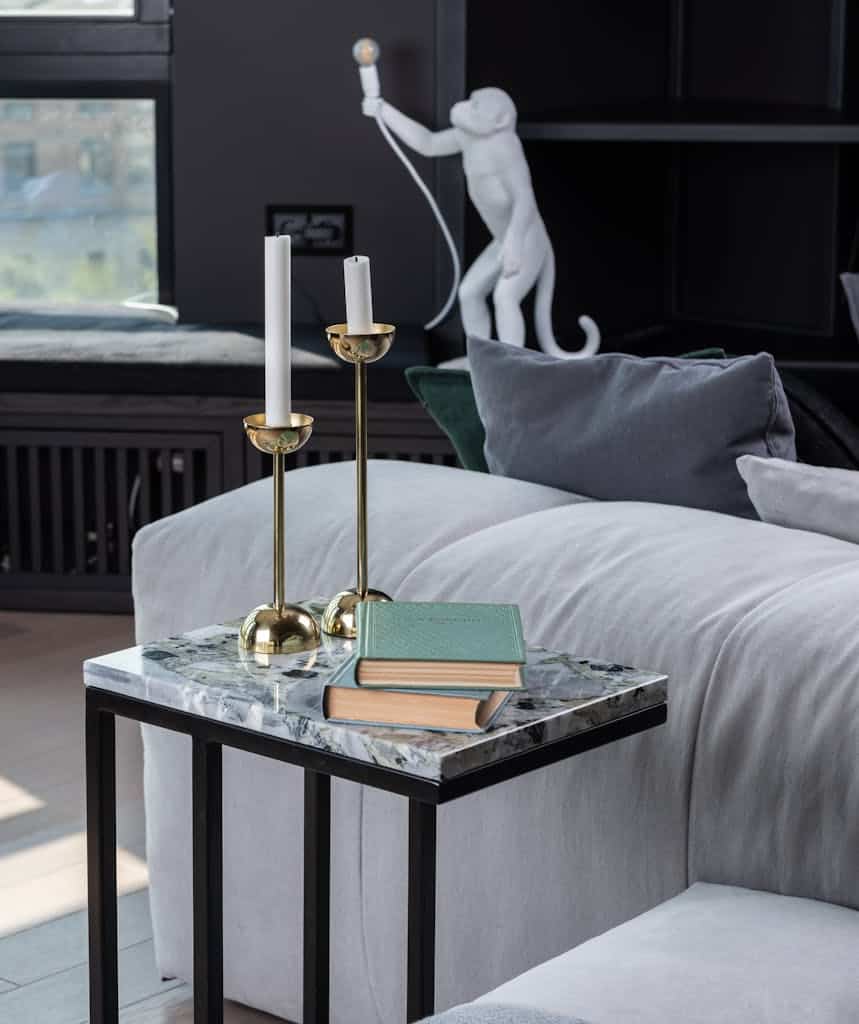 Books and candlesticks on marble coffee table in cozy living room near gray comfortable sofa