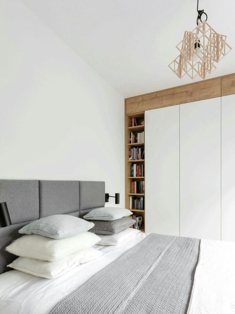 A full-wall built-in wardrobe with handle-free doors next to the bed, along the wall. Only a sleek wooden niche is visible in the corner., with wooden shelves to create some playfulness and texture in the room.