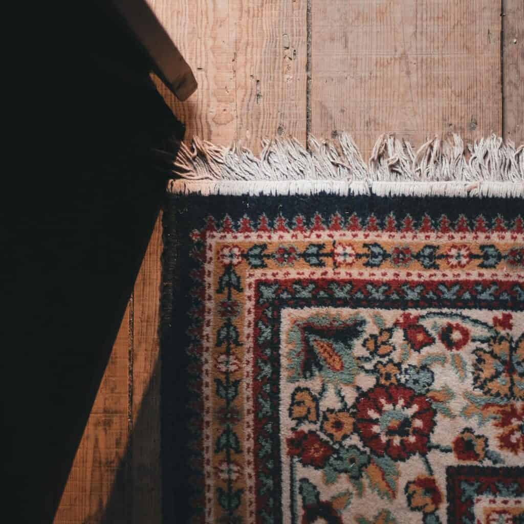 From above part of ornamental carpet with white fringe placed on aged wooden floor in daylight