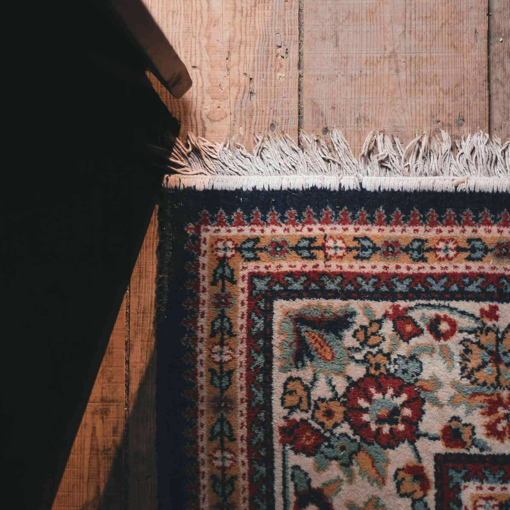 From above part of ornamental carpet with white fringe placed on aged wooden floor in daylight