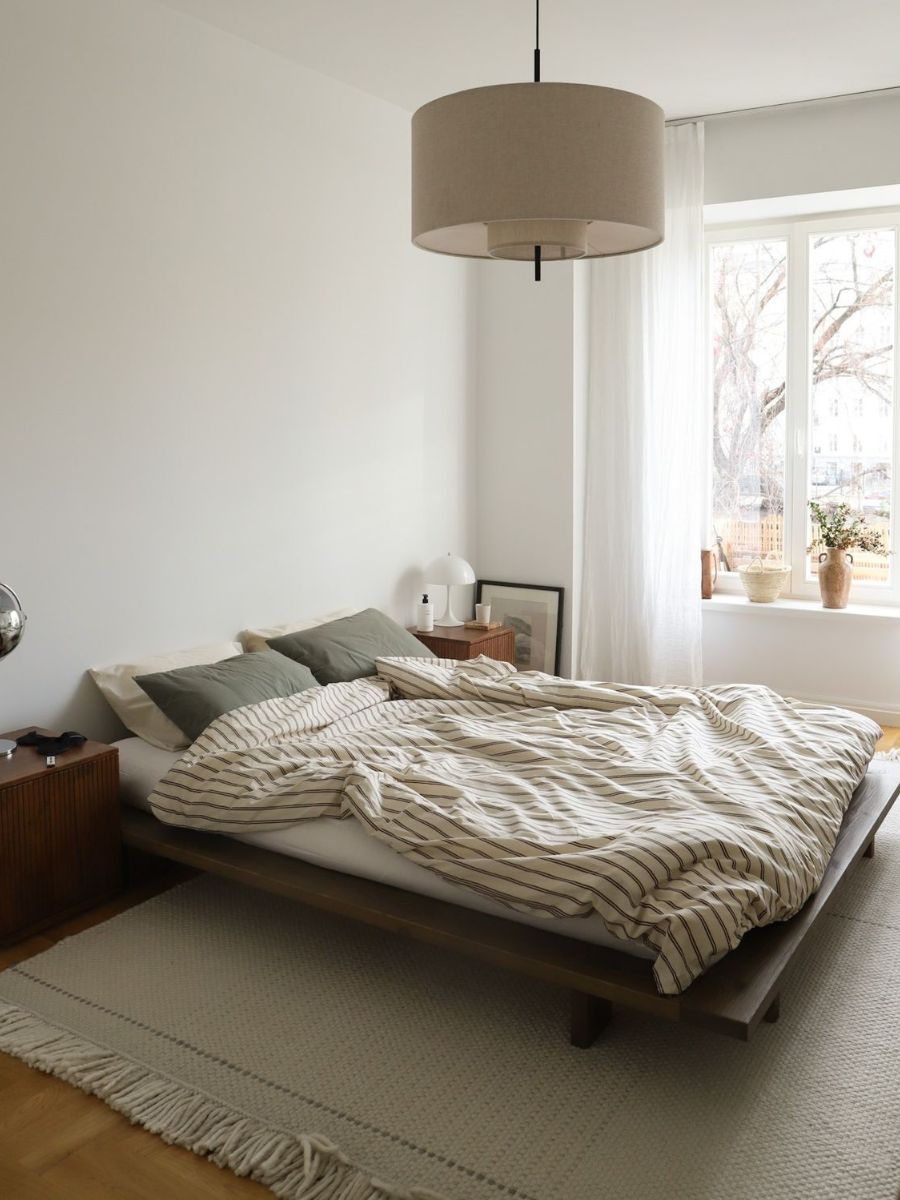 Correctly sized rug in a small bedroom extending beyond the sides and foot of the bed. Shot in diffused morning light, minimal styling — plain bedding, one lamp.