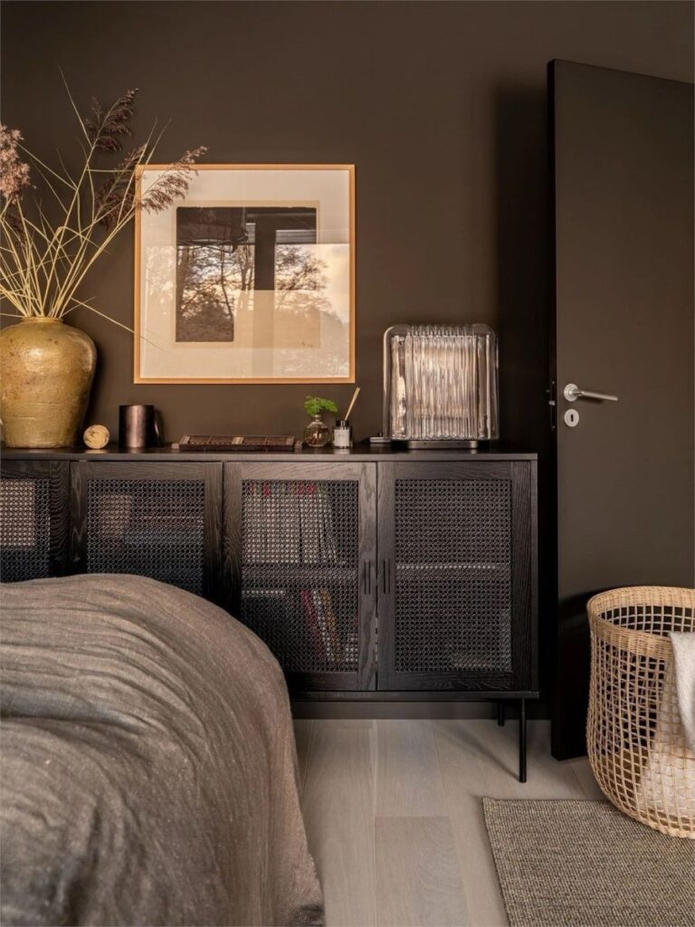 Dark bedroom detail, a black wooden small cabinet with art on top, representing storage in a small bedroom.