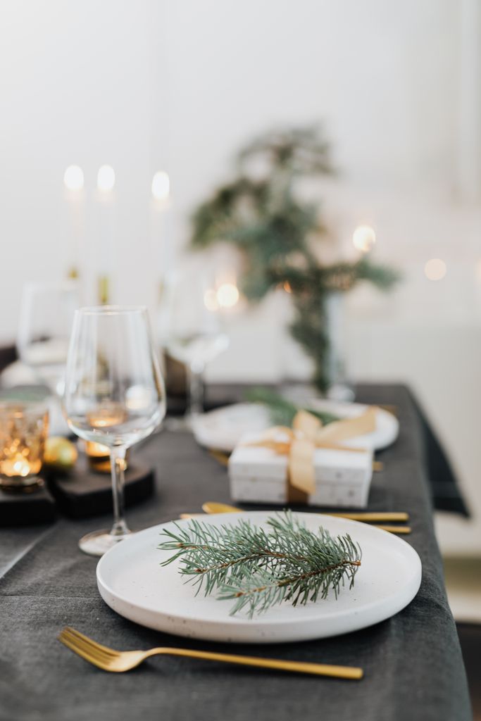 Festive table setting with pine twigs, candles, and gift-wrapped presents.